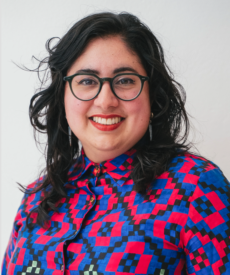 Parveen D smiling with a white background wearing glasses and a lively printed collared shirt.